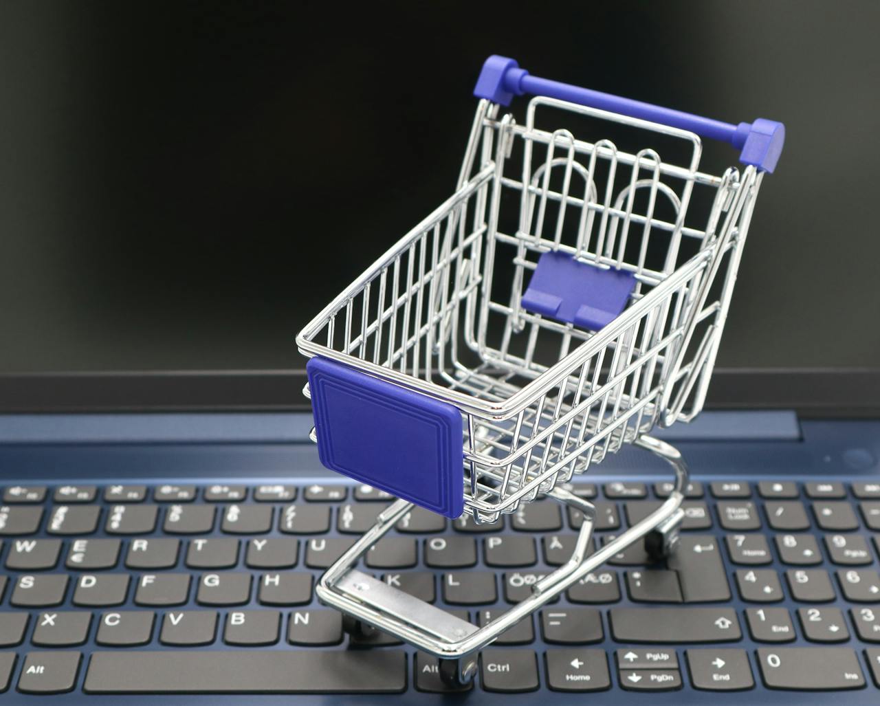 hero-img-01 A mini shopping cart placed on a laptop keyboard, symbolizing online shopping and digital retail.